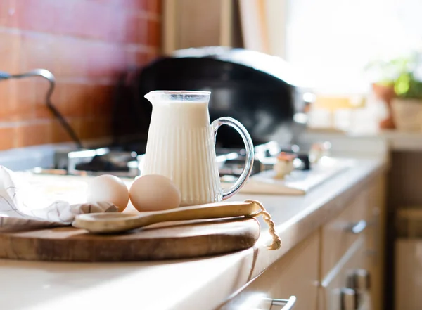 Свежее молоко и яйца на деревянной доске в реальном интерьере кухни дома с естественным освещением — стоковое фото