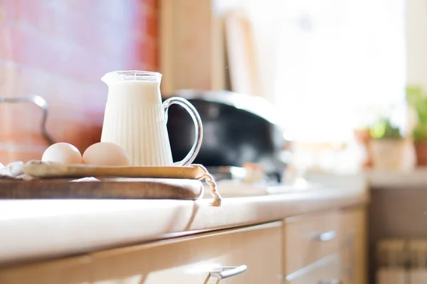 Свежее молоко и яйца на деревянной доске в реальном интерьере кухни дома с естественным освещением — стоковое фото