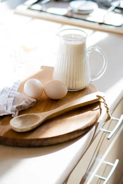 Leche fresca y huevos en tablero de madera en el interior de la cocina casera real con luz natural — Foto de Stock