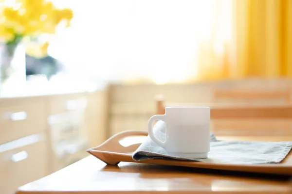 Weiße Kaffeetasse mit Serviette auf dem Tisch in echtem Kücheninterieur mit hellem Tageslicht — Stockfoto