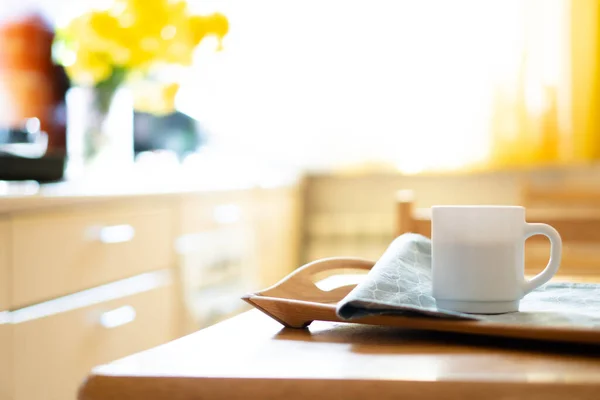 Bílý hrnek na kávu s ubrouskem na stole v reálném kuchyňském interiéru s jasným přírodním slunečním světlem — Stock fotografie