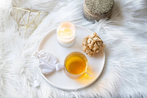 Taza de té de hierbas y vela ardiente en bandeja decorativa redonda blanca — Foto de Stock