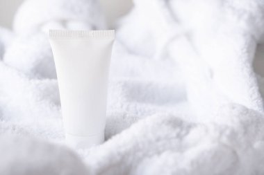 Kabarık beyaz pamuklu havlu arka planında temiz beyaz kozmetik krem tüpü, model ve tasarım hazır.