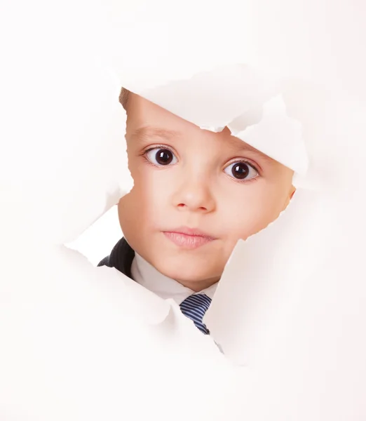 Serious kid looks through a hole in paper — Stock Photo, Image