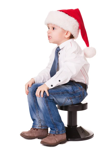 Angry kid in santa hat on chair — Stock Photo, Image