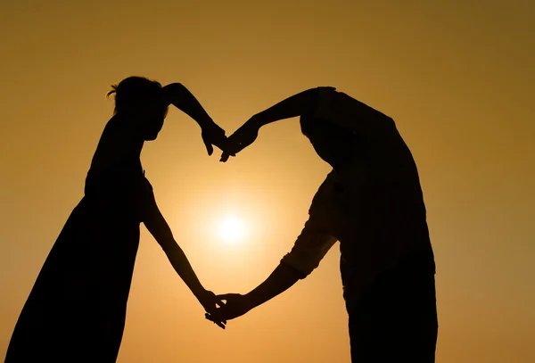 Sillhouette casal amoroso ao pôr do sol com o coração — Fotografia de Stock