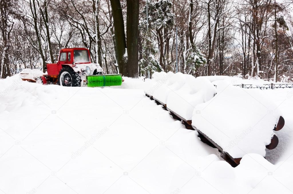Red tractor cleaning park after snowfall