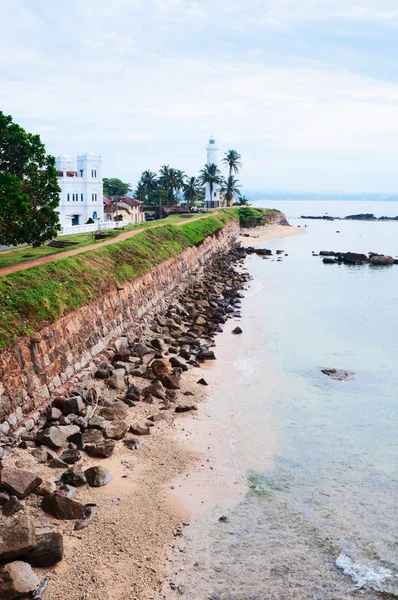 Sea shore with high wall and white lighthouse — Stock Photo, Image