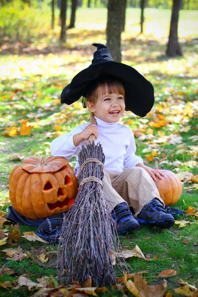 Piccolo ragazzo sorridente con zucche di Halloween, una scopa e un cappello — Foto Stock