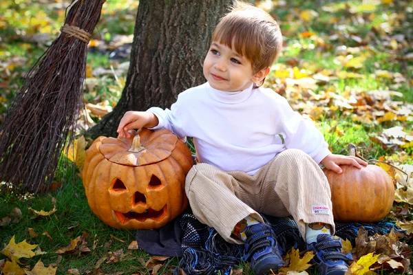 Little smiling boy with two halloween pumpkins and a broom sitti — Stock Photo, Image