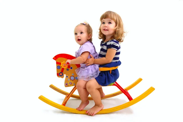 Two little girls on a wooden horse isolated on white background — Stock Photo, Image