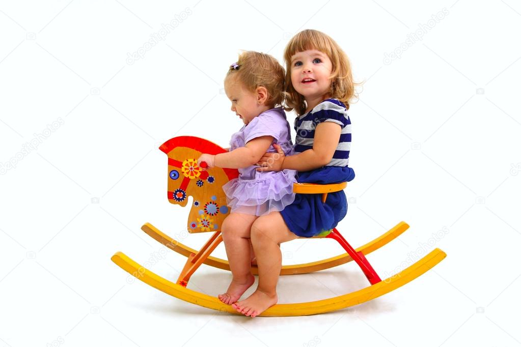 Two happy little girls riding on a toy wooden horse isolated on
