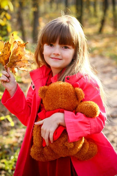 Akçaağaç yaprakları ve bir oyuncak ayı ile gülümseyen kız — Stok fotoğraf