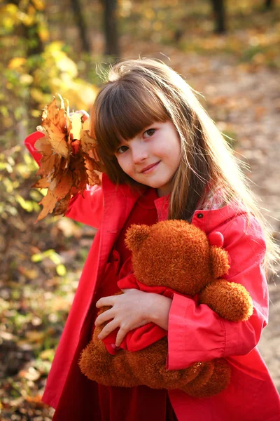 Liten flicka i skogen höst med lönn blad och teddy — Stockfoto