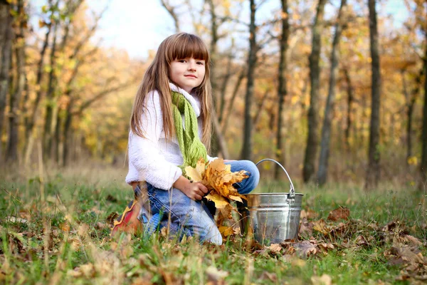 Girl with yellow leaves and a bucket outdoors — Stock Photo, Image