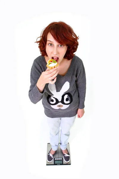 Fille debout sur la balance et manger du gâteau isolé sur ba blanc — Photo