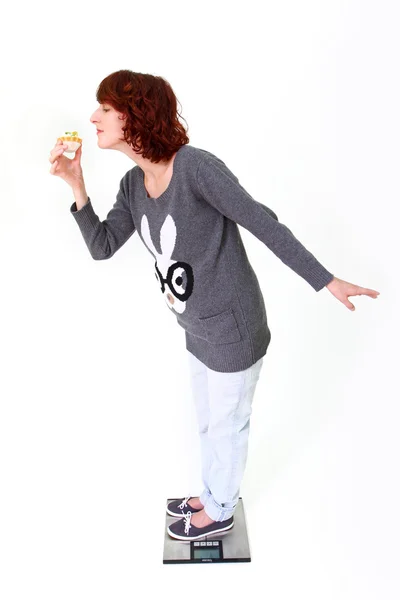 Beautiful girl standing on the scale and holding a cake — Stock Photo, Image