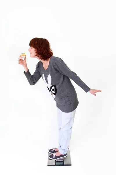 Fat young woman standing on the scale and holding a cake — Stock Photo, Image