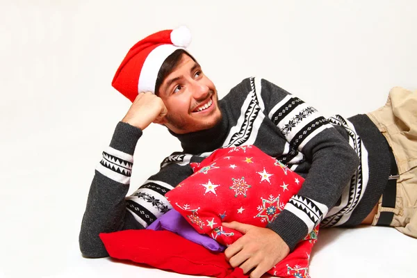 Smiling young man wearing a Santa Claus hat with pillows isolate — Stock Photo, Image