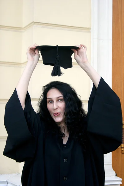 Young student in gown near the university trying on the cap — Stock Photo, Image