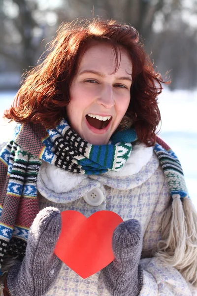 Happy girl holding a red heart on the background of a winter par — Stock Photo, Image