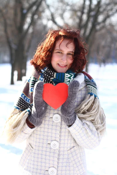 Inverno sorrindo jovem mulher segurando um coração vermelho ao ar livre — Fotografia de Stock