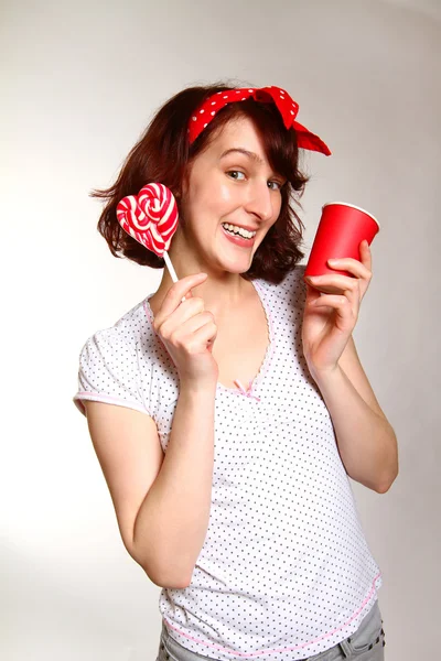 Lächelnde junge Frau mit einem Lutscher und einer Tasse posiert isoliert auf — Stockfoto