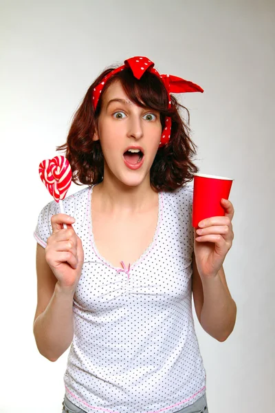 Surprised girl with a lollipop and a cup isolated on a gray back — Stock Photo, Image