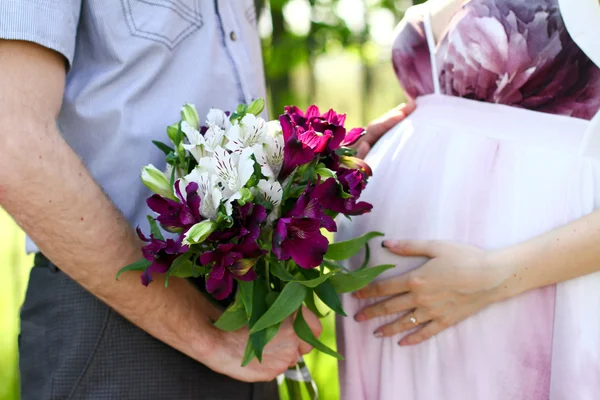 Gravida par med bukett blommor i en sommar park — Stockfoto