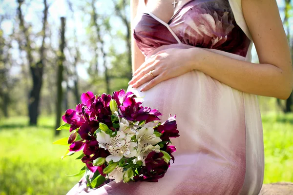 Pregnant woman with a bouquet of flowers in a summer park — Stock Photo, Image