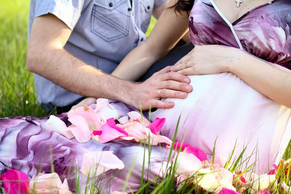 幸せな妊娠中のカップルにバラの花びらを持つ草の上に座って、 — ストック写真