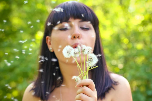 Attractive young woman blowing on a dandelion in the summer park Royalty Free Stock Images