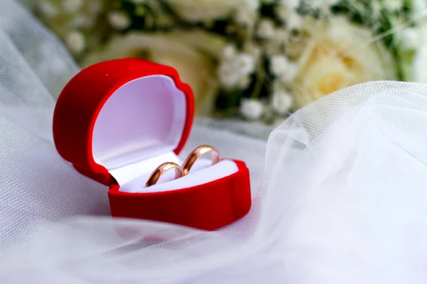 Anillos de boda en una caja roja y un primer plano de ramo — Foto de Stock