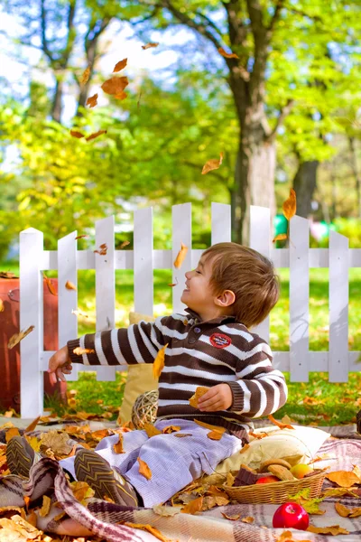 Liten pojke leker med blad och äta kakor i höst — Stockfoto