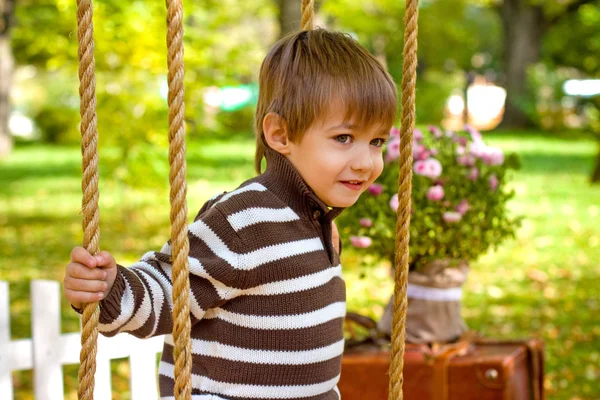 Menino sentado em um balanço no parque de outono — Fotografia de Stock