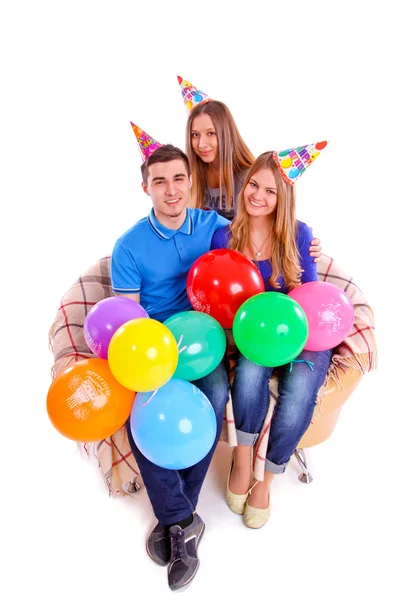 Drei Freunde sitzen auf einer Couch mit Hüten und Luftballons — Stockfoto