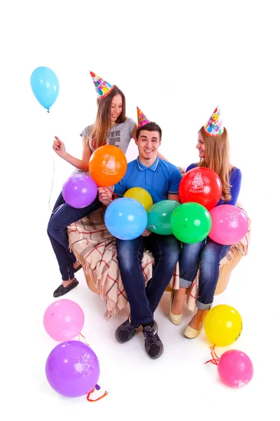 Drei Freunde mit Hüten und Luftballons sitzen auf der Couch — Stockfoto
