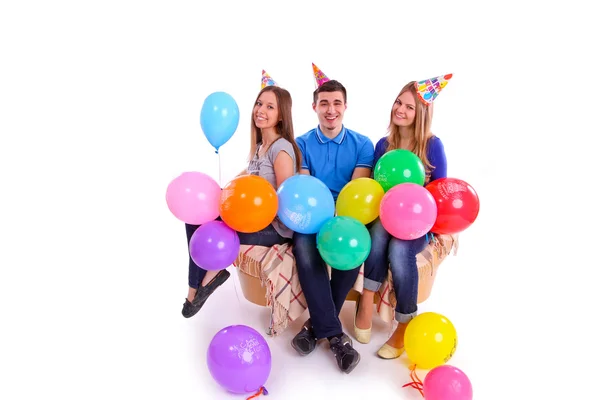 Tres amigos sentados en un sofá con globos y sombreros —  Fotos de Stock