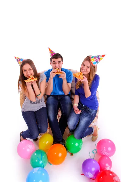 Three friends with hats and balloons eating pizza — Stock Photo, Image