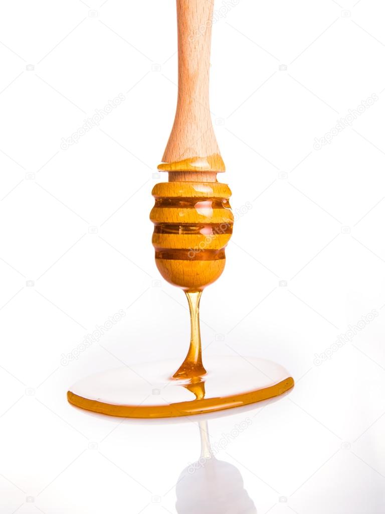 Honey drip from wooden dipper on white background