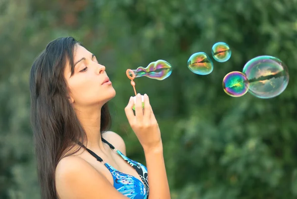 Portrait of attractive young girl inflating colorful soap bubbles in nature — Stock Photo, Image