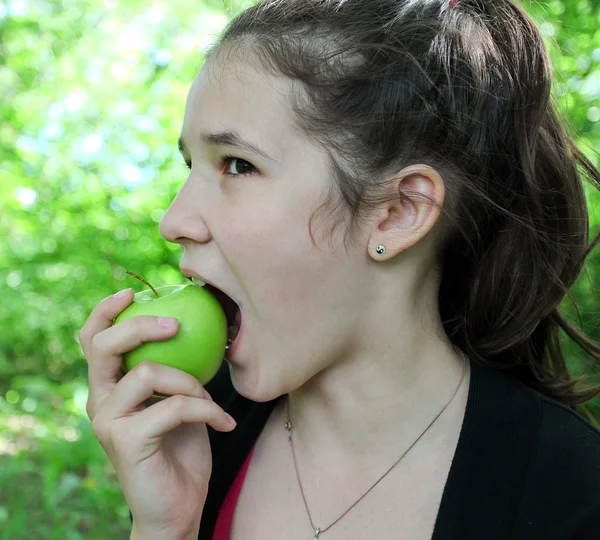 Brunette young girl eating apple in summer park — Stock Photo, Image