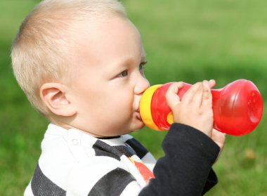 Beautiful little boy drinking from red bottle