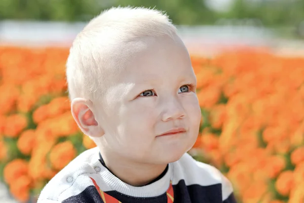 Young cheerful baby over bright flowers in park — Stock Photo, Image