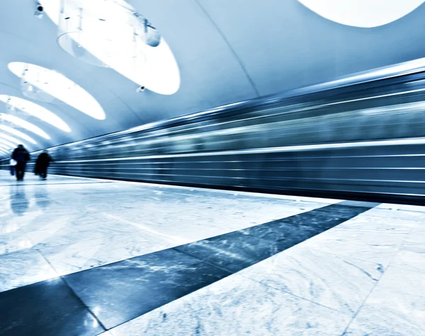 Perspective wide angle view of modern light blue illuminated and spacious public metro marble station with fast blurred trail of train in vanishing traffic motion — Stock Photo, Image