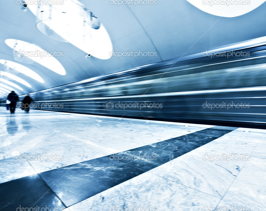 Perspective wide angle view of modern light blue illuminated and spacious public metro marble station with fast blurred trail of train in vanishing traffic motion