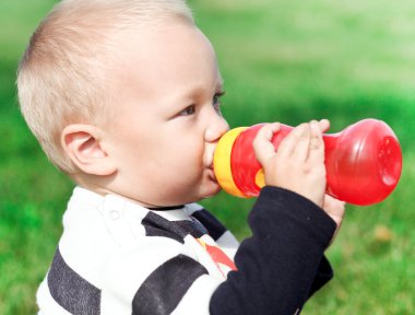 beautiful little boy drinking from red bottle