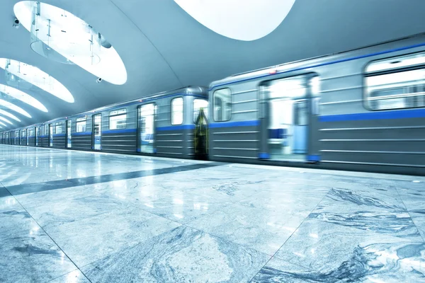 Perspective wide angle view of modern light blue illuminated and spacious public metro marble station with fast blurred trail of train in vanishing traffic motion — Stock Photo, Image