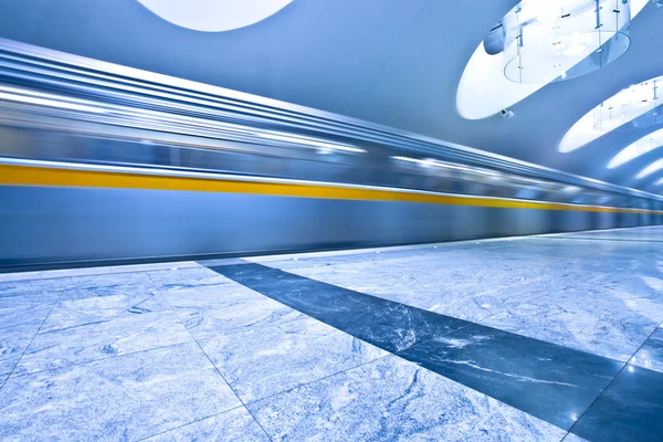 Perspective wide angle view of modern light blue illuminated and spacious public metro marble station with fast blurred trail of train in vanishing traffic motion — Stock Photo, Image