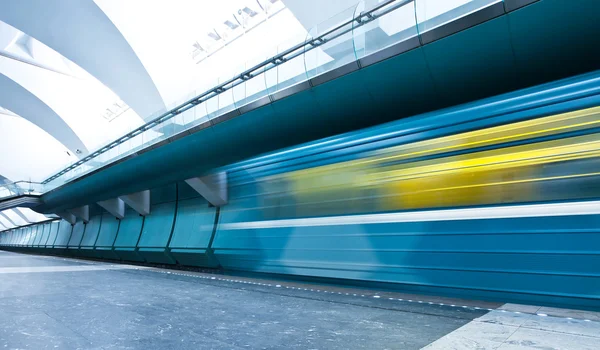 Perspective wide angle view of modern light blue illuminated and spacious public metro marble station with fast blurred trail of train in vanishing traffic motion Stock Photo